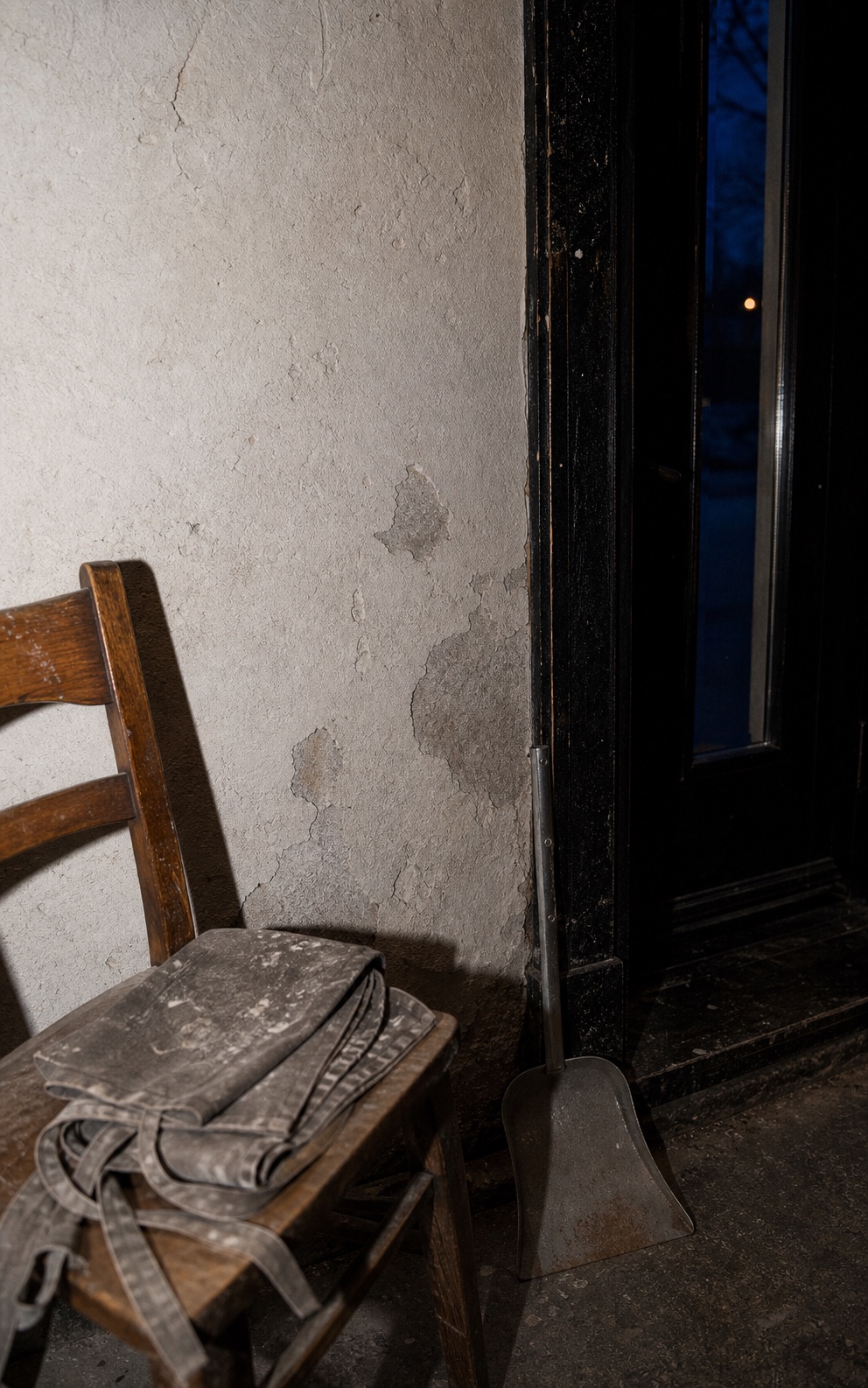 A flour-dusted apron on a chair beside a metal dustpan and the café's black service door