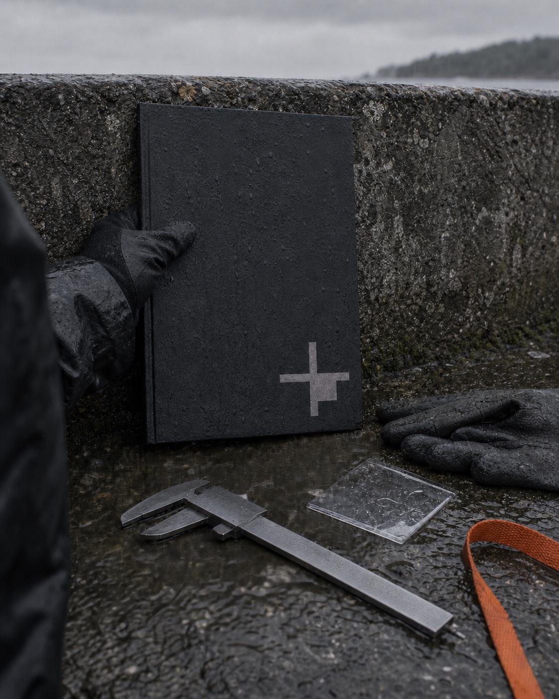 A gloved researcher holding a wet black folio carrying the GROUND datum mark