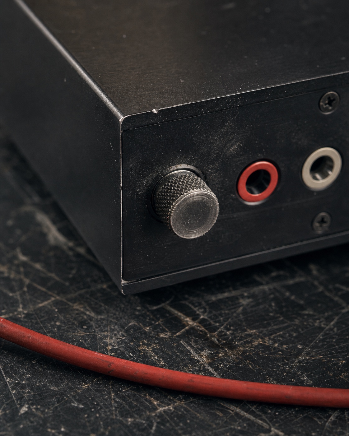 A close view of a worn black instrument corner, knurled control, ports, screws, and red cable